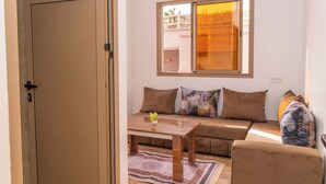 A living room with a sofa, a coffee table, and a window with a view of buildings. - TIFAWINE STAY IMSOAUNE SURF AND YOUGA (Imsouane)