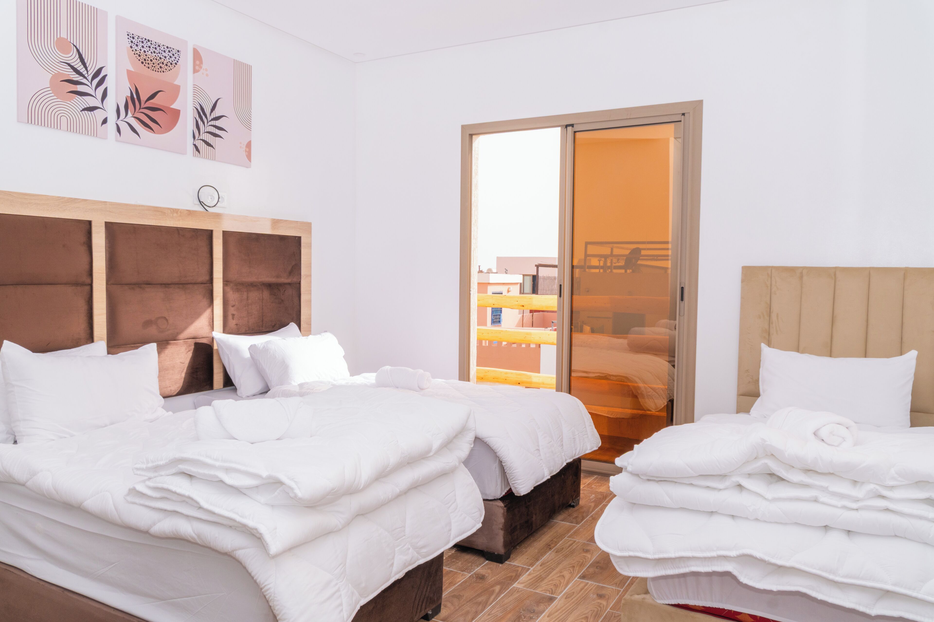 A hotel room with two beds, a sliding glass door to the balcony, and artwork on the wall.