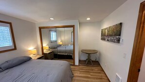 Un dormitorio con cama, lámparas de noche, una mesita, un espejo y un cuadro en la pared.