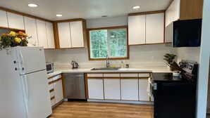 Una cocina moderna con armarios de madera, lavavajillas integrado, refrigerador, fregadero y ventana que proporciona luz natural.
