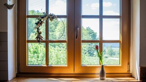 Una ventana con vistas a follaje, un florero con una flor y un adorno colgante.