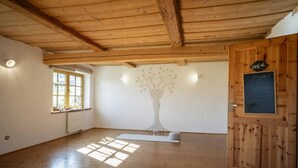 Habitación con pisos de madera, un ventanal grande, un mural de un árbol en la pared y una puerta con una pizarra.