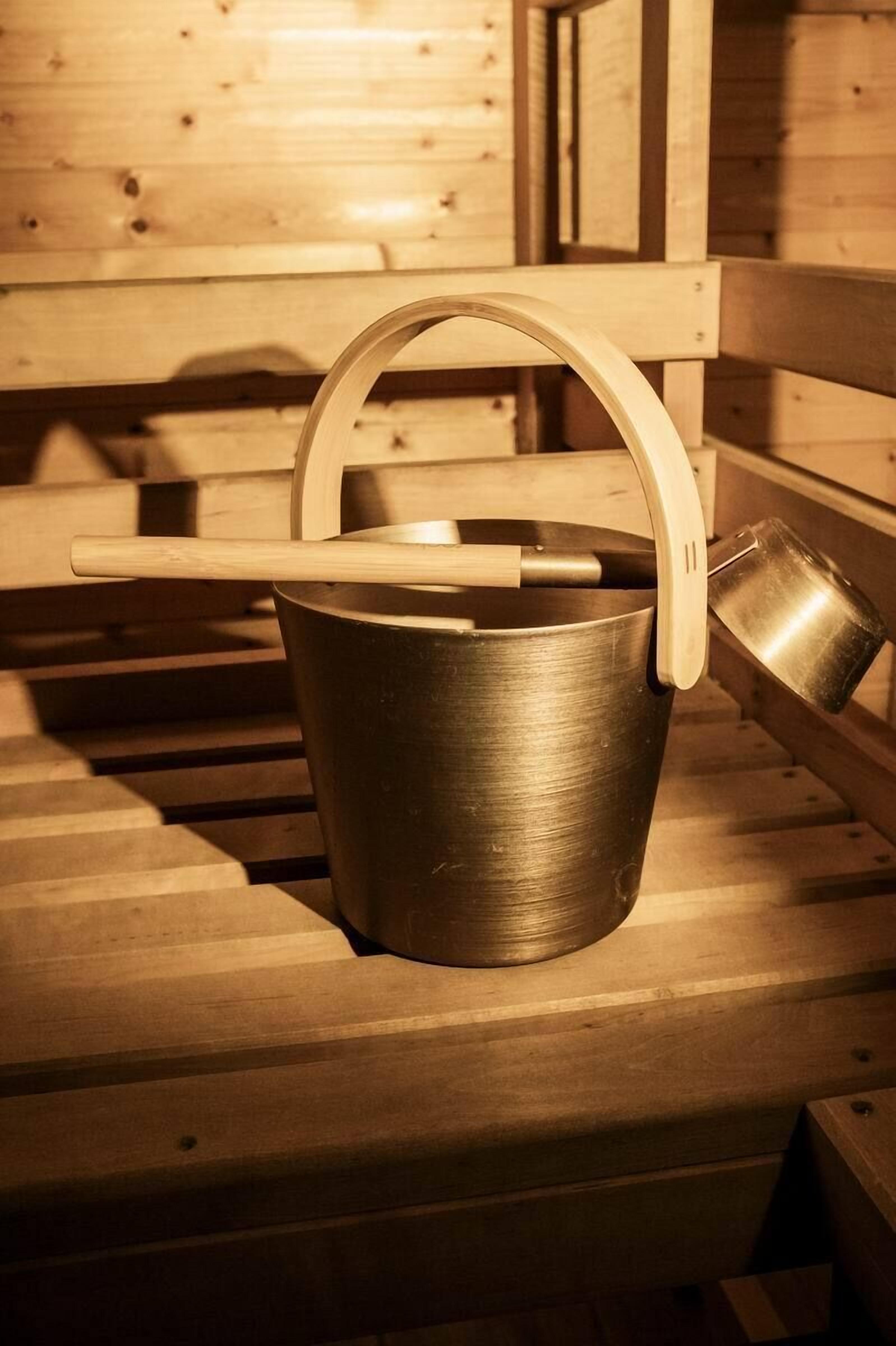 Een metalen emmer met een houten handvat op een houten bank.