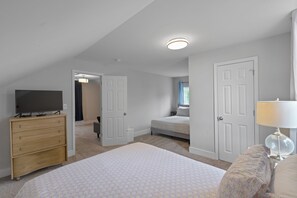 Ein Schlafzimmer mit Bett, Kommode, Fernseher und einer Tür zu einem weiteren Raum.