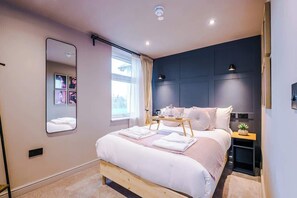 Een moderne slaapkamer met een groot bed, nachtkastjes, een spiegel en een raam met gordijnen.