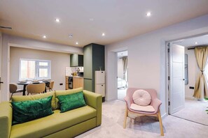 Een moderne woonkamer met een groene bank, een roze fauteuil en een eethoek met een tafel en stoelen.