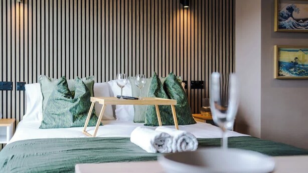 A hotel room with a bed, a bedside table with a tray, glasses, and a bowl.