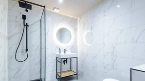 A modern bathroom with a glass-enclosed shower, a round mirror above a white sink, and a toilet.