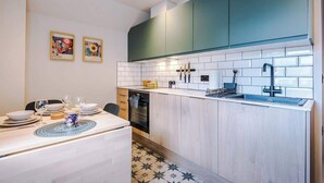 Cocina compacta con gabinetes color turquesa, azulejos blancos y un comedor con mesa para dos.