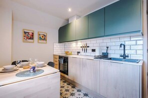Een compacte keuken met blauwgroene kastjes, witte tegels en een eethoek met een tafel gedekt voor twee personen.