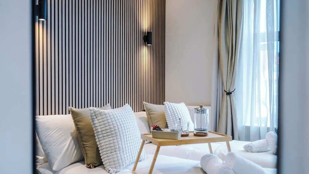 Una habitación de hotel moderna con una cama, almohadas, una mesita de noche con una bandeja y toallas.