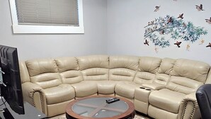 A living room with a beige sectional sofa, a round coffee table, a flat-screen TV, and a wall-mounted artwork.