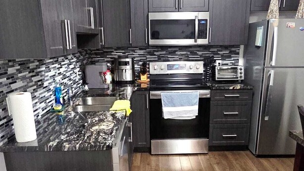 A modern kitchen with dark cabinets, a stainless steel microwave, oven, and refrigerator.