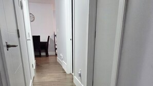 A narrow hallway with wooden flooring, white walls, and a door on the right.