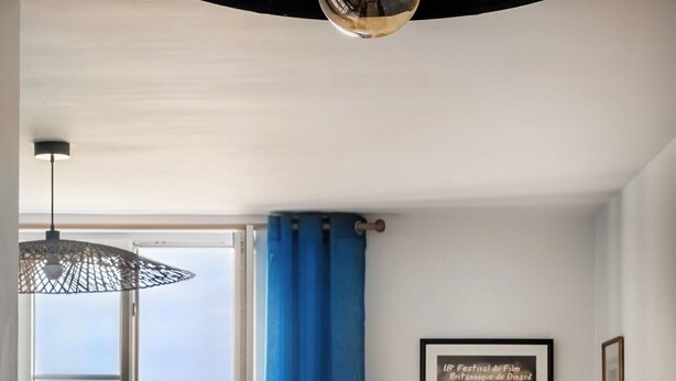Een eetgedeelte met uitzicht op zee, een gedekte tafel met glazen en een schaal, en een poster aan de muur.