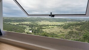 A view from a window with a triangular frame, overlooking a green landscape with trees and a river.