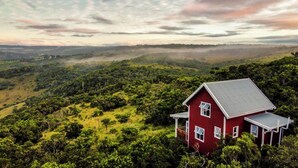 A red house with a sloped roof, surrounded by lush greenery and hills.