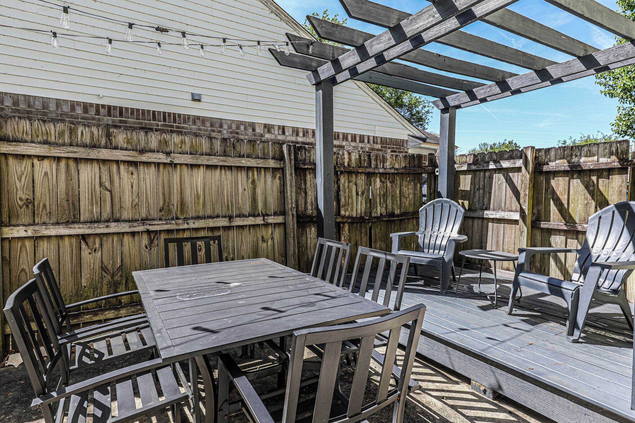 Um deck de madeira com pérgola, uma mesa e cadeiras.