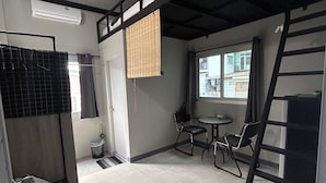 A room with a bunk bed, a small table with chairs, a window with a view, and a towel rack. - Munchies Bed&Breakfast (Bangkok)