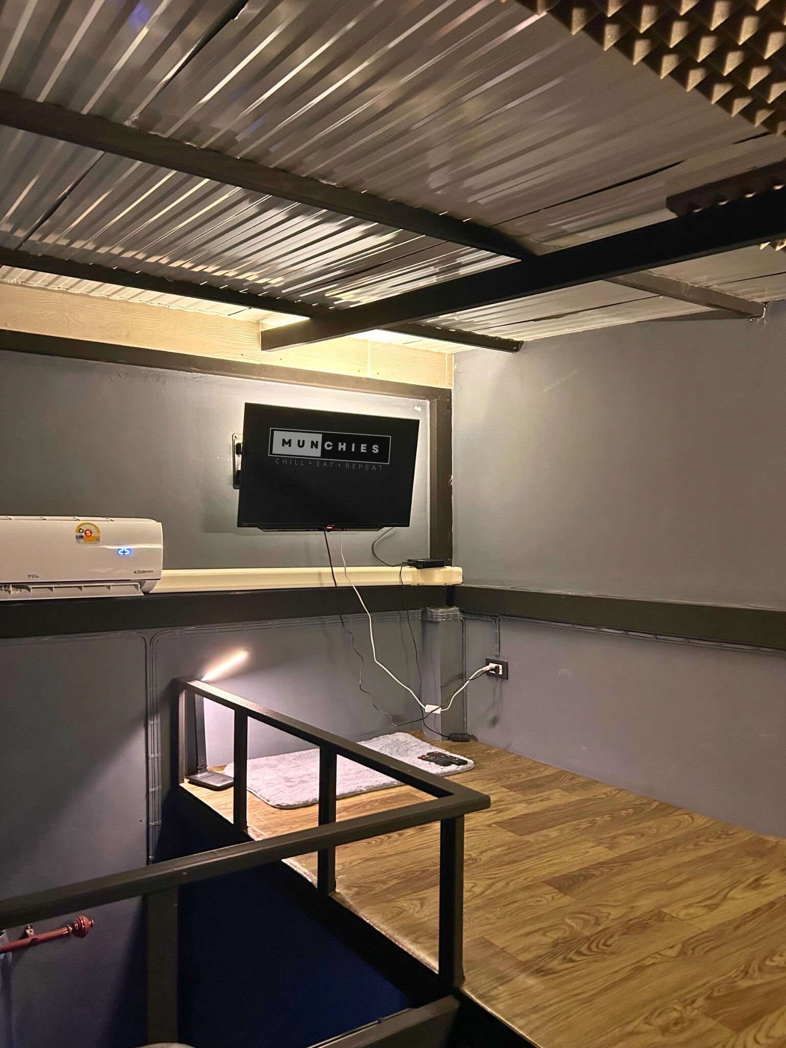 A compact room with a mounted TV, a small table, and a ceiling vent.