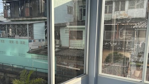 A room with large windows overlooking a residential area, a balcony with a railing, and a potted plant. - Munchies Bed&Breakfast (Bangkok)