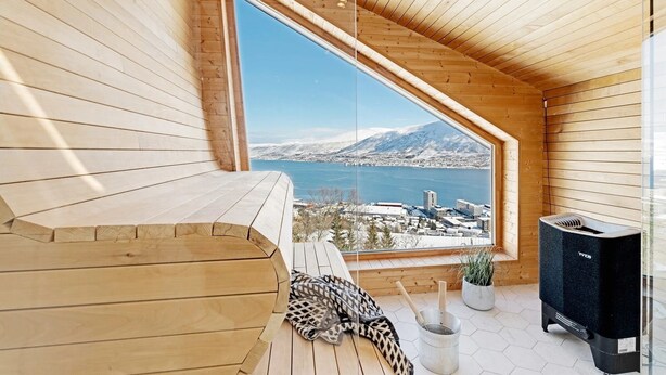 A wooden interior with a large window offering a view of a city and mountains. - Deluxe Villa by Paramount (Troms)