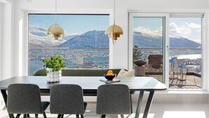 A dining area with a table, chairs, and a view of a city and mountains through large windows. - Deluxe Villa by Paramount (Troms)