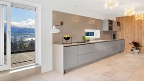 A modern kitchen with a large island, a built-in oven, and a view of a snowy mountain through a sliding door. - Deluxe Villa by Paramount (Troms)