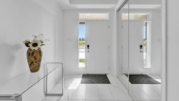 Un pasillo moderno con barandilla de vidrio, un jarrón decorativo con flores y una puerta que da al exterior.