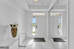 A modern hallway with a glass railing, a decorative vase with flowers, and a door leading outside.