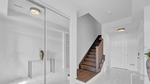 Un interior moderno con entrada de puerta de cristal, una escalera de madera y una puerta blanca.