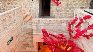 A stone building with a central arched doorway, a small window, and a staircase leading to an upper level. - MİRİSSO KONAK HOTEL MARDİN ARTUKLU (Mardin)
