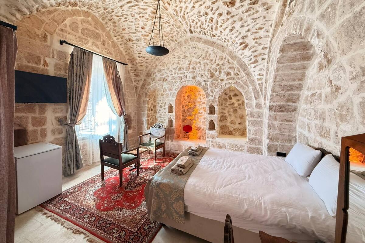 A stone-walled bedroom with a bed, a desk, and a chair.