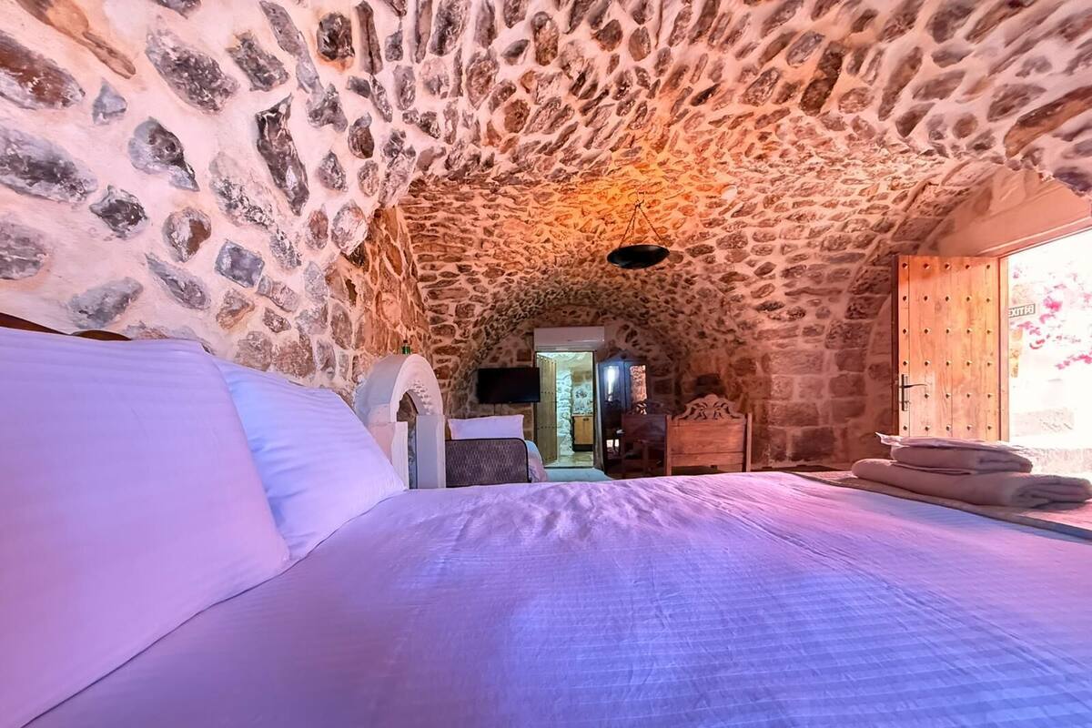 A stone-walled bedroom with a bed, a wooden wardrobe, and a television.
