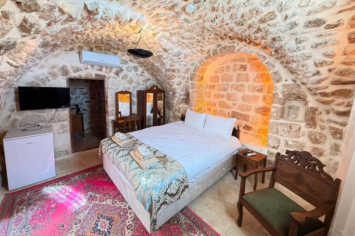 A stone-walled bedroom with a bed, a television, and a small table.