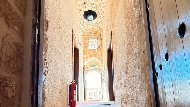 A narrow, stone-walled corridor with a wooden door on the right, leading to a staircase and an exit sign. - MİRİSSO KONAK HOTEL MARDİN ARTUKLU (Mardin)