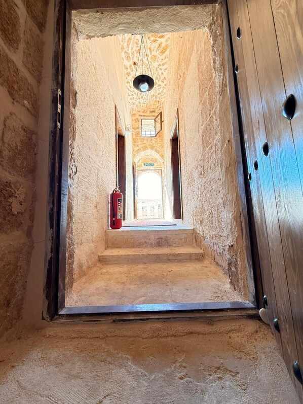 A narrow, stone-walled corridor with a wooden door on the right, leading to a staircase and an exit sign. - MİRİSSO KONAK HOTEL MARDİN ARTUKLU (Mardin)
