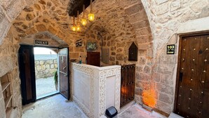 A stone-walled interior with a reception desk, an exit sign, and a door marked '103'. - MİRİSSO KONAK HOTEL MARDİN ARTUKLU (Mardin)