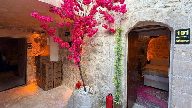 A stone-walled interior with a pink flowering plant, a fire extinguisher, and a room number sign. - MİRİSSO KONAK HOTEL MARDİN ARTUKLU (Mardin)