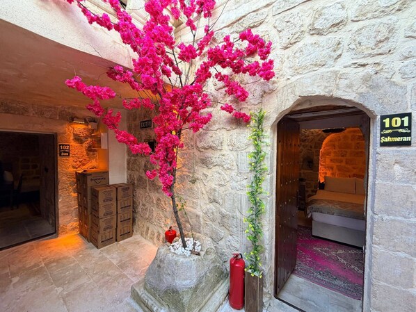 A stone-walled interior with a pink flowering plant, a fire extinguisher, and a room number sign. - MİRİSSO KONAK HOTEL MARDİN ARTUKLU (Mardin)