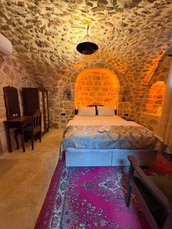 Une pièce avec un plafond en pierre, un lit avec une literie à motifs, un bureau avec des chaises et un grand tapis.