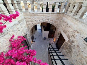 A stone corridor with a staircase leading to a door, surrounded by stone walls and pink flowers.