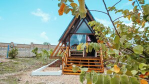 A small, triangular wooden structure with a glass window, surrounded by greenery and a clear sky. - leoglampingznz (Nungwi)
