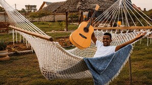 A hammock with a guitar, set in a grassy area with a thatched-roof structure in the background. - leoglampingznz (Nungwi)