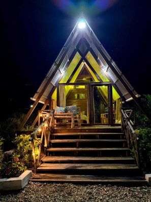 A triangular wooden structure with a staircase leading to an entrance, surrounded by plants. - Leo Cabin (Nungwi)