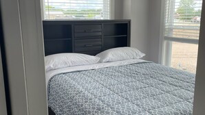 Een slaapkamer met een bed, een donker hoofdeinde en een raam met zonwering.