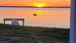 Zonsondergang uitzicht vanaf een grasrijk gebied met een steiger en een tafel, uitkijkend op kalm water.
