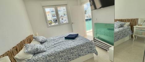 Un dormitorio con cama, televisor, ventana y espejo.