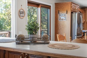 Una cocina con armarios de madera, un refrigerador de acero inoxidable, una planta en maceta y un cartel de bienvenida.