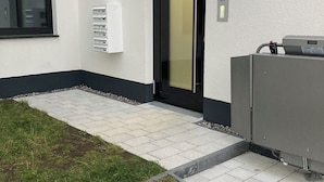 Una entrada de edificio con una puerta negra, un ventanal y un cuadro eléctrico.